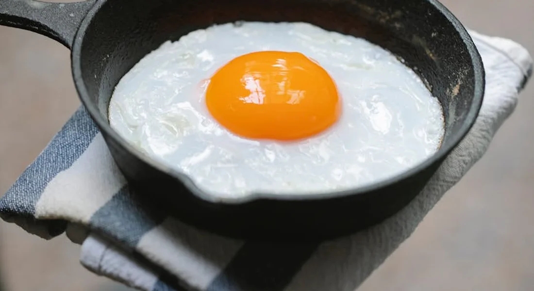 Cast iron skillet with a sunny-side-up egg resting on a white surface on top of a striped cloth