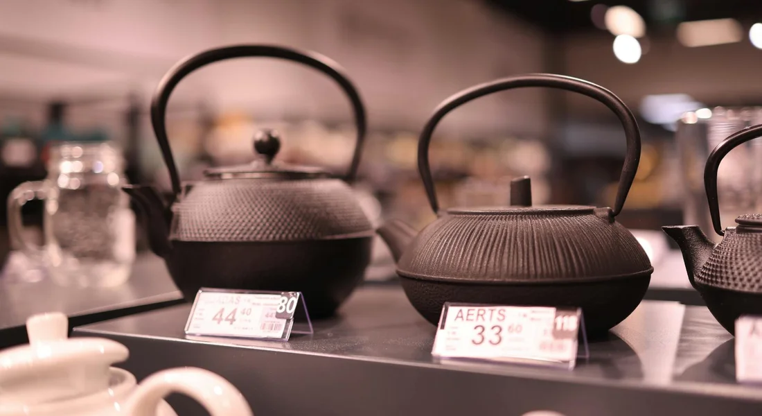 Several black cast iron teapots on a store display with price tags.