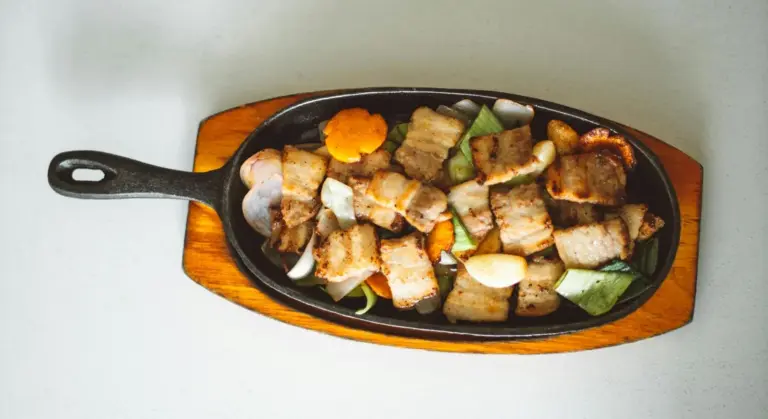Cast iron skillet filled with roasted pork and vegetables on a wooden serving board.