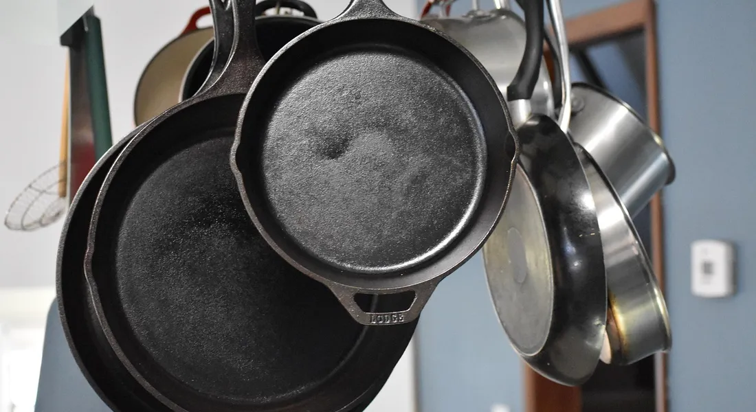 A collection of cast iron skillets and pots hanging from a rack in a kitchen.