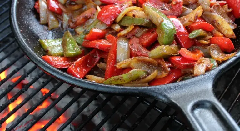 Cast iron skillet with colorful sautéed peppers and onions cooking on a charcoal grill.