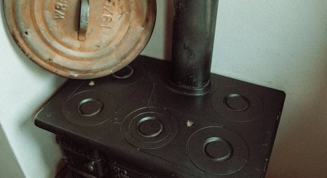 Close-up of a black cast-iron stove with circular hot plates and a rusted lid on the left