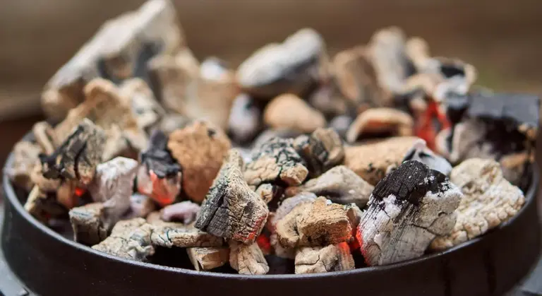 Close-up of glowing charcoal briquettes in a round cast-iron pan, ready for heating.