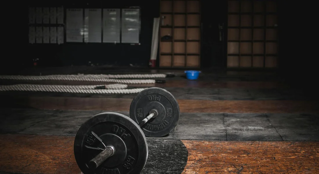 Two cast-iron dumbbells resting on a worn wooden gym floor in a dimly lit training room.
