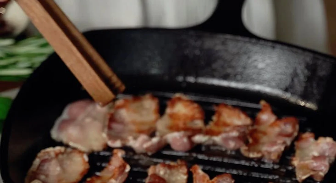 Meat slices sticking to a hot cast-iron grill pan with a wooden chopstick resting on the edge
