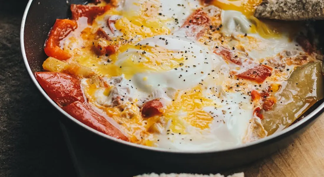 A cast-iron skillet with sunny-side-up eggs and sautéed peppers, illustrating the egg-skillet break-in process