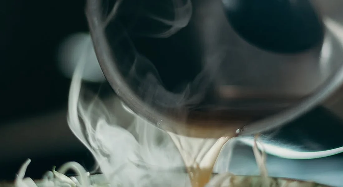 Close-up of steam rising from a pour of hot liquid from an enameled cast iron pot, highlighting careful handling.