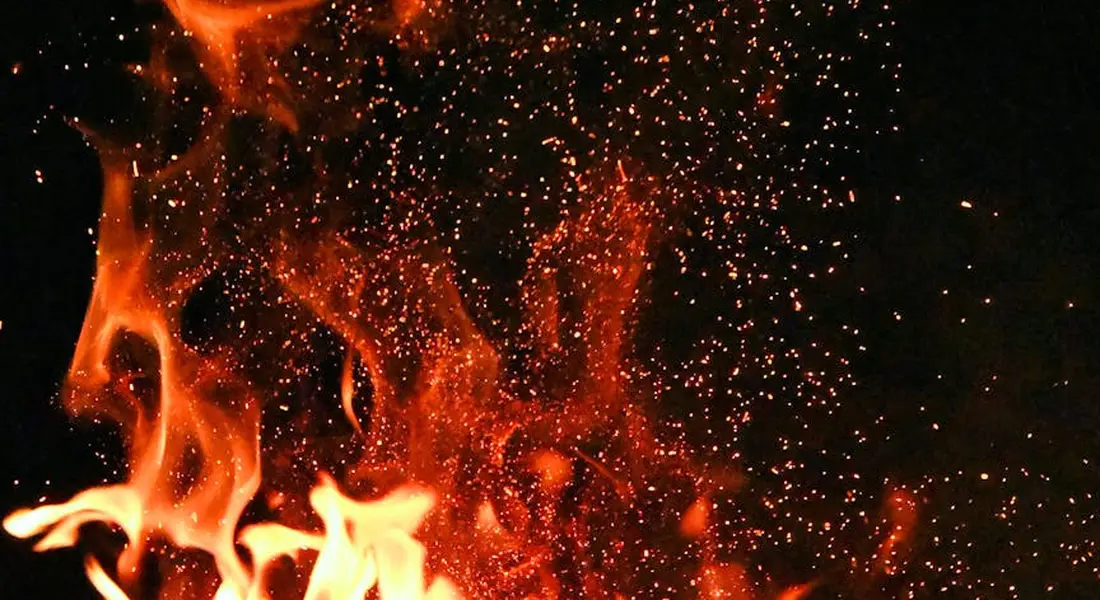 Close-up of bright orange flames and embers against a dark background