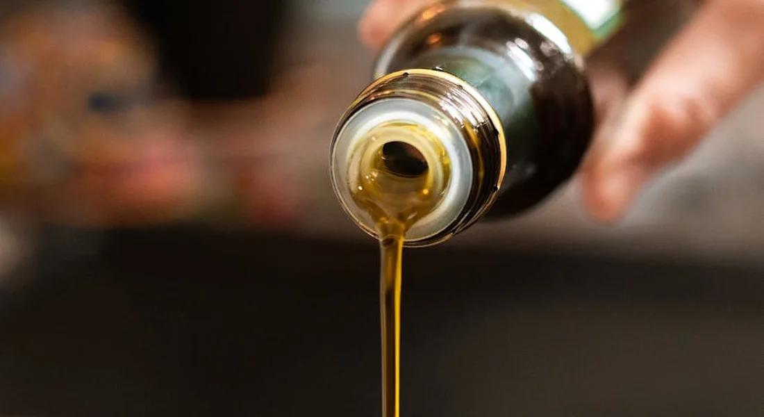 Close-up of golden flaxseed oil pouring from a bottle with a blurred kitchen background