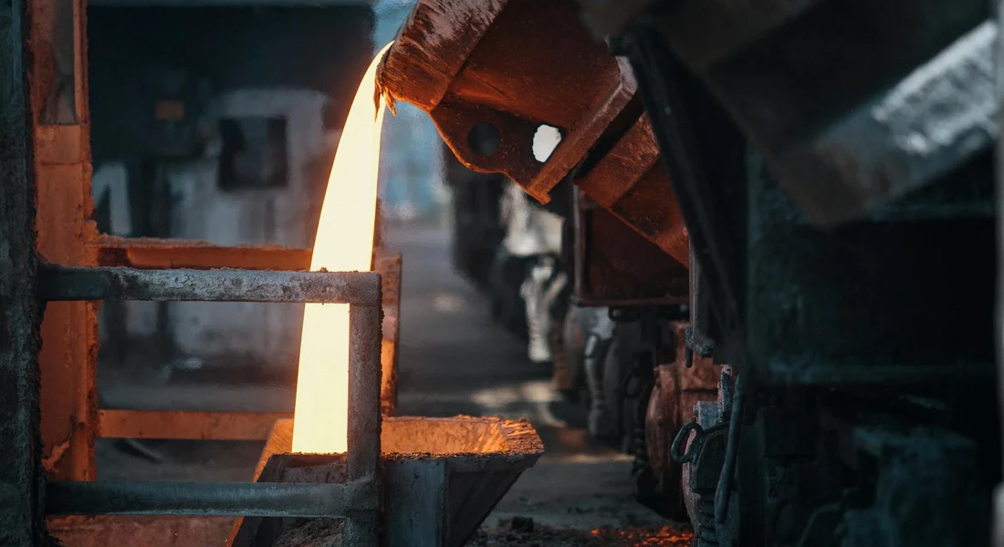 Close-up of molten iron pouring from a furnace into a mold in a busy foundry.