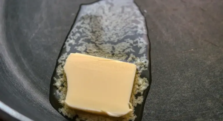 Square pat of butter on the bottom of a dark baking pan, with a light dusting of flour to help grease the surface.
