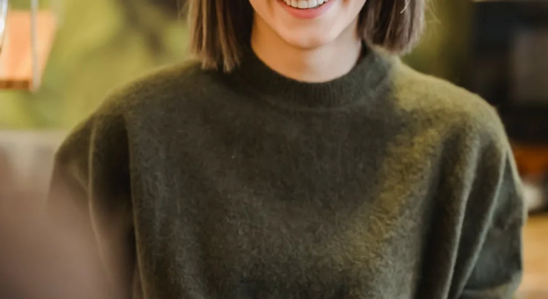 Close-up of a person wearing a dark green sweater, cropped at the shoulders, smiling softly.