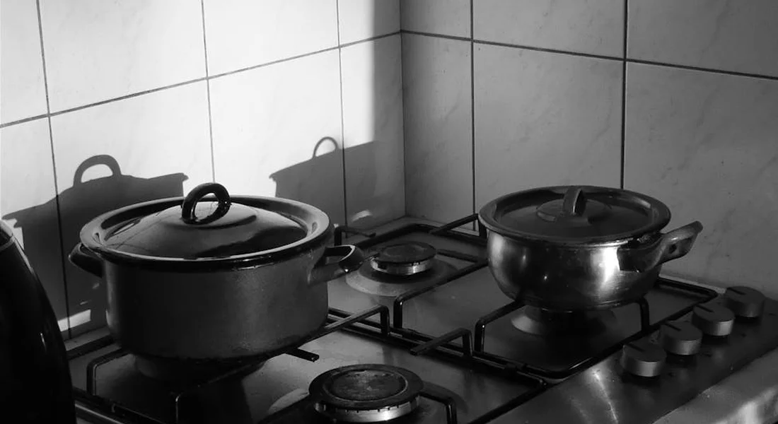 Black-and-white photo of a gas stove with two pots on the burners and a tiled backsplash