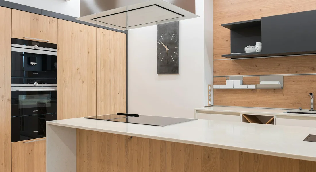 Modern kitchen with a wooden island and a smooth electric cooktop; built-in ovens and a clock on the wall.