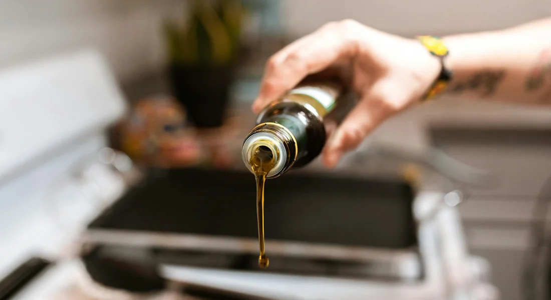 Close-up of a hand pouring oil from a bottle into a hot seasoned skillet to prevent rust.