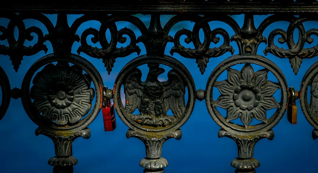Close-up of decorative cast-iron circular motifs on a railing with floral and sunburst patterns against a bright blue sky.