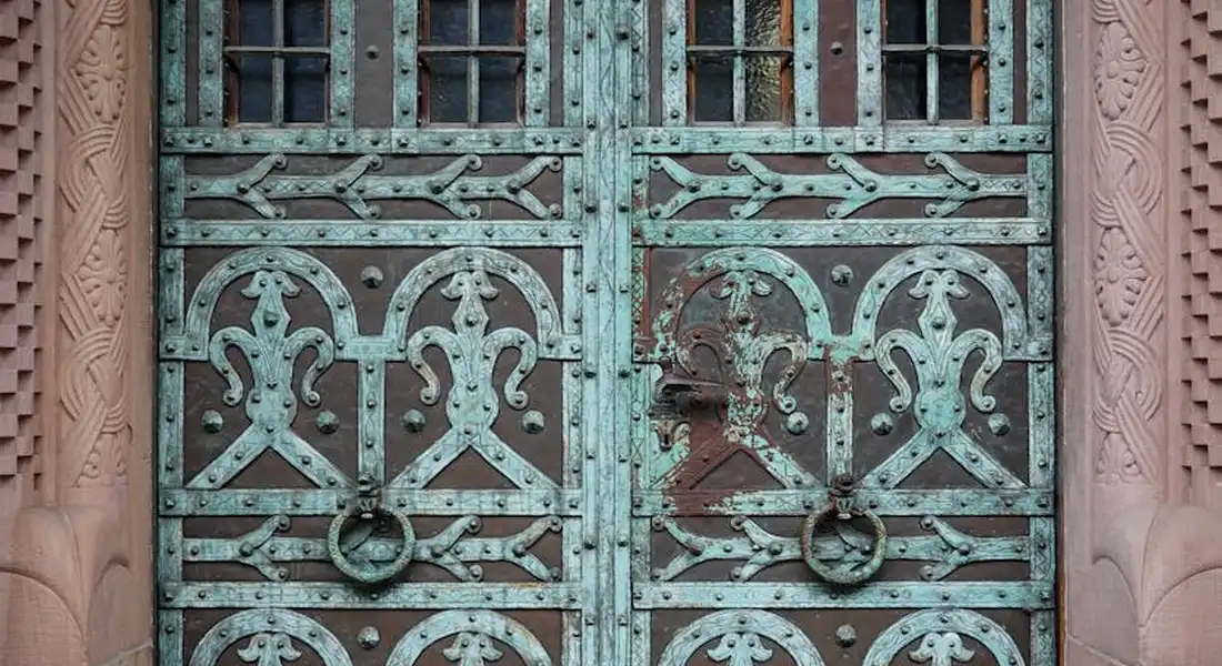 Decorative turquoise iron gate with intricate scrollwork and circular ring handles