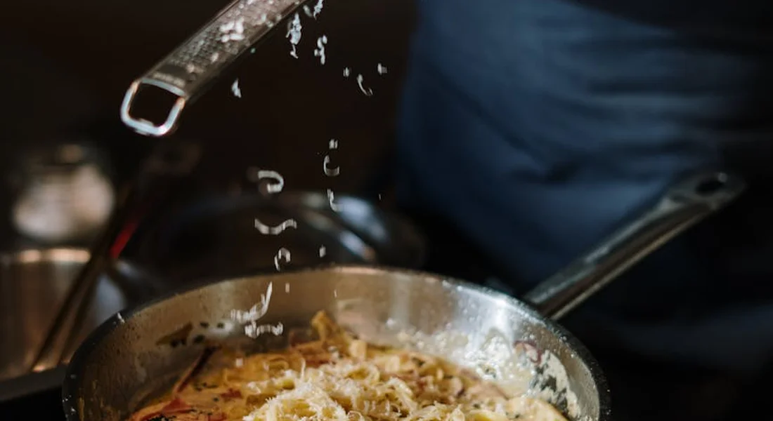 Close-up of a frying pan on a stove with food cooking, droplets of liquid splattering into the air.