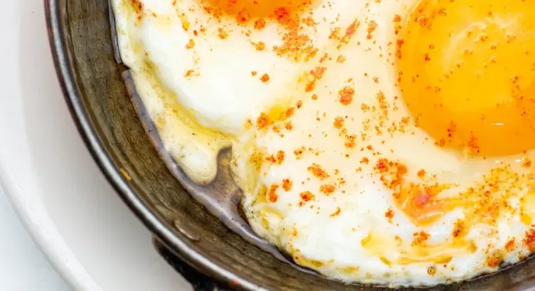 Close-up of sunny-side-up eggs frying in a skillet with paprika sprinkled on top, illustrating a nonstick pan in use.