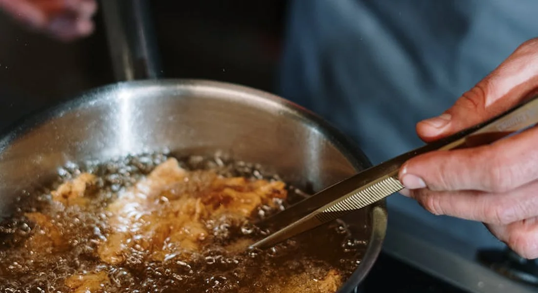 Close-up of a stovetop skillet being used with tongs, oil sizzling, illustrating everyday use of a seasoned pan.