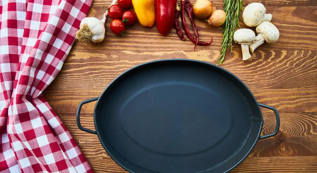 Cast iron skillet on a wooden countertop with fresh vegetables and a red checkered cloth nearby.