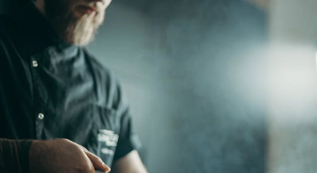 A person in a dark shirt stands in a moody kitchen with a blue-gray backdrop, suggesting careful inspection of cookware.