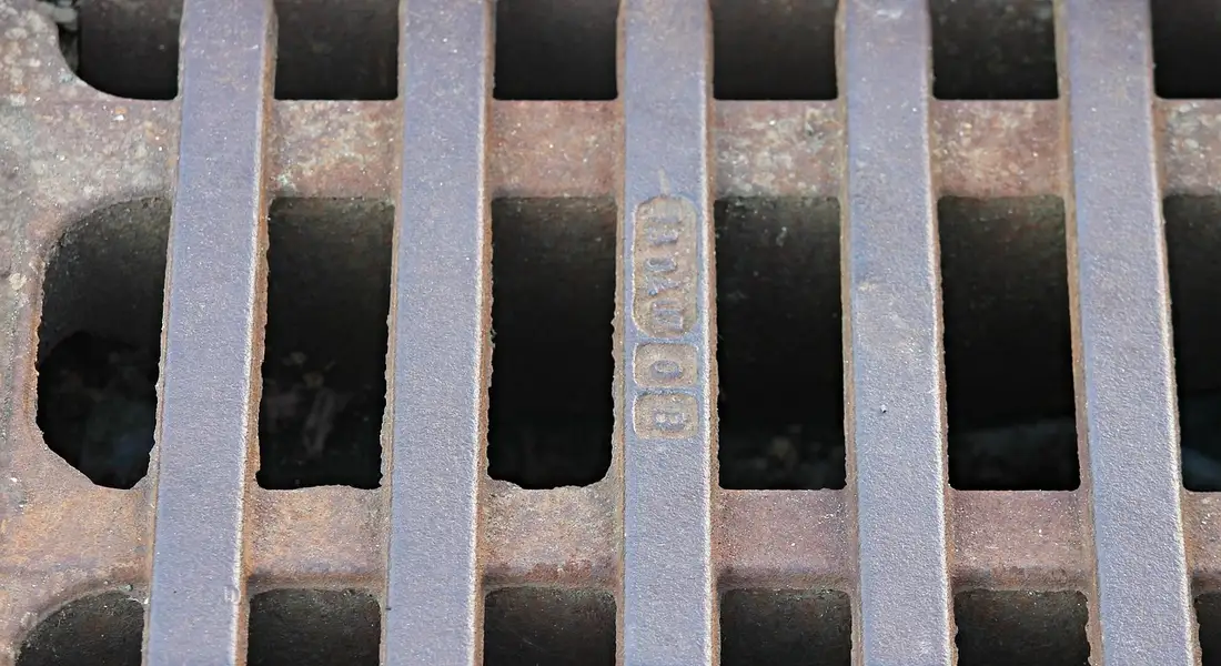 Close-up of a metal drain grate with vertical bars and dark gaps