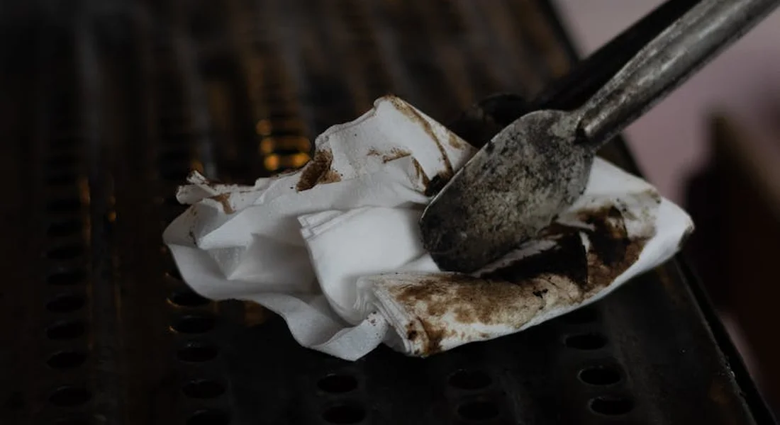 Close-up of a rust-stained cast iron grill grate with a metal scraper and crumpled paper towel
