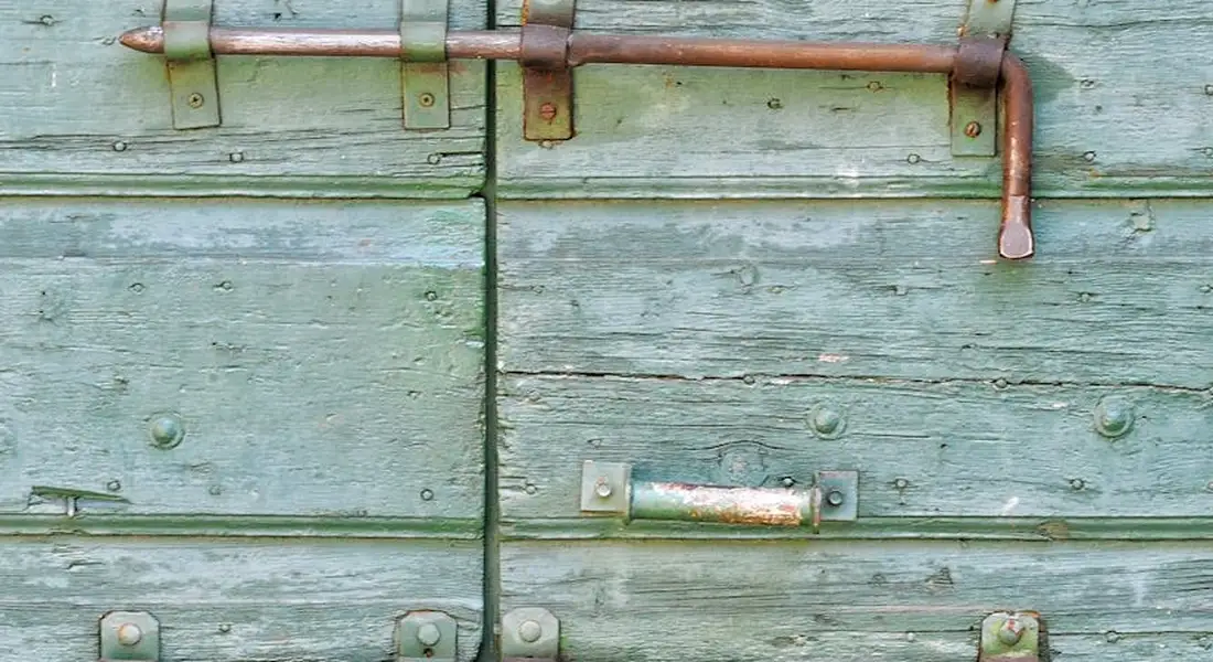 Close-up of a weathered green wooden door with rusted metal hardware, illustrating rust removal challenges.