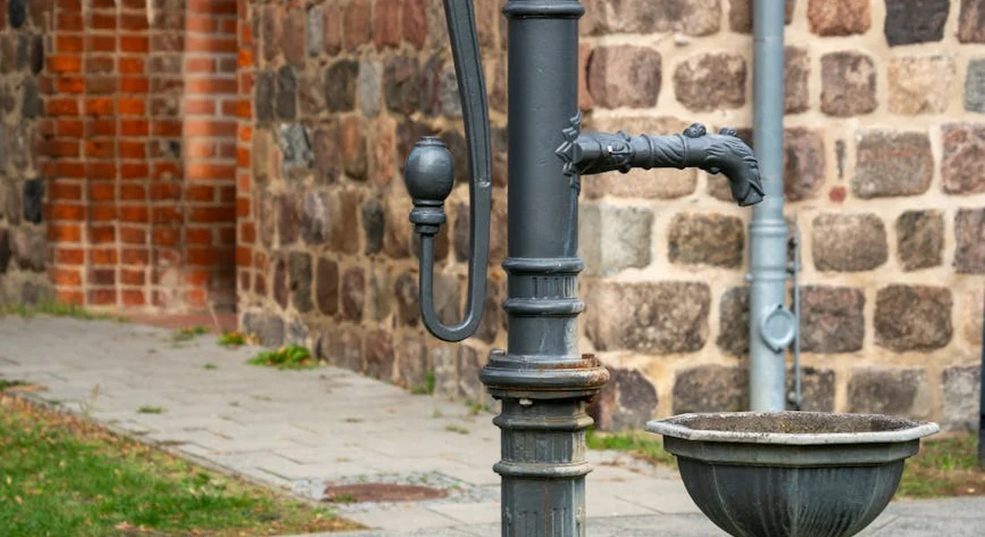 Cast iron water pump against a brick wall with visible rust on the metalwork