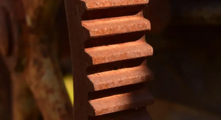 Close-up of a rusted cast iron gear showing orange-brown oxide layers