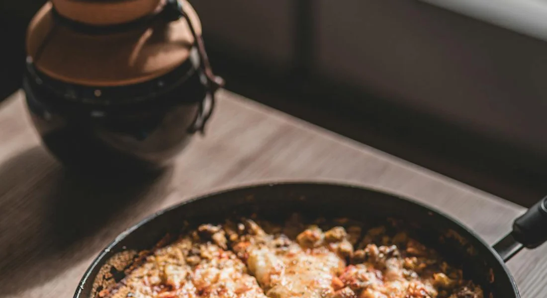 Cast iron skillet on a stovetop with a savory dish cooking, a ceramic jar in the background.