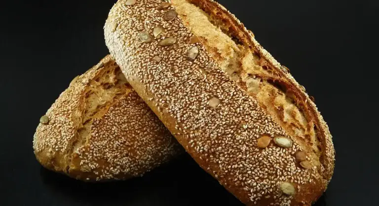 Two sesame-seed crusted loaves on a dark background