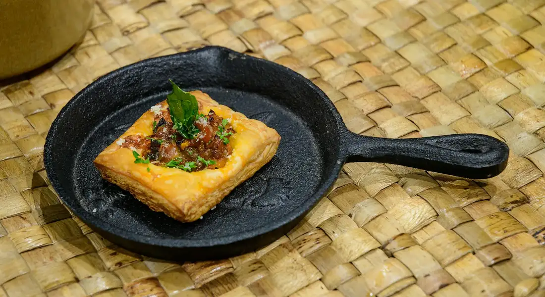 A small cast iron skillet on a woven mat with a single square pastry inside.