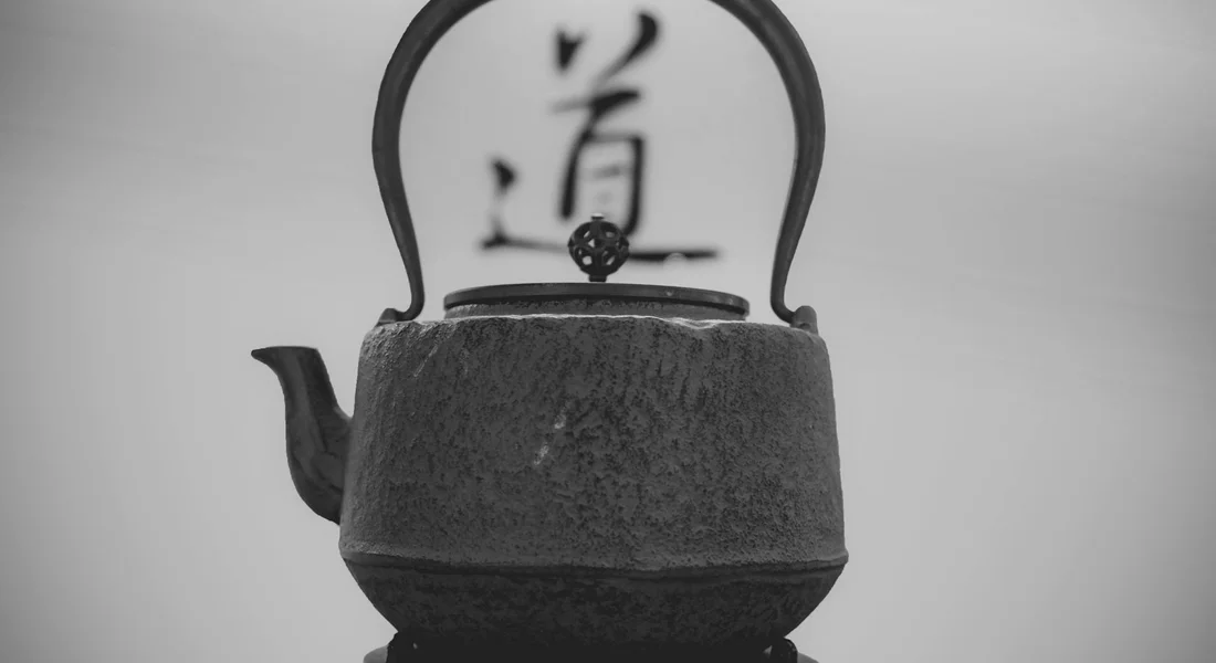 Black cast-iron teapot with a curved handle on a stovetop, with a blurred background featuring calligraphic characters.