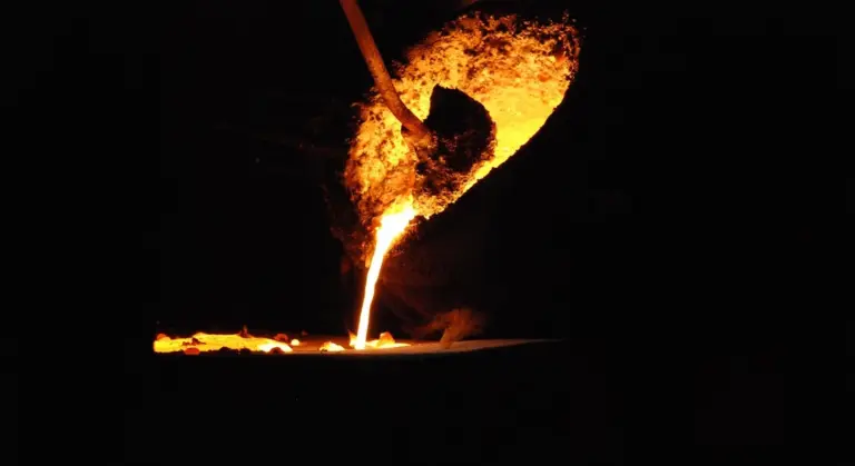 Molten iron pours from a crucible into a mold, glowing orange against a dark background.