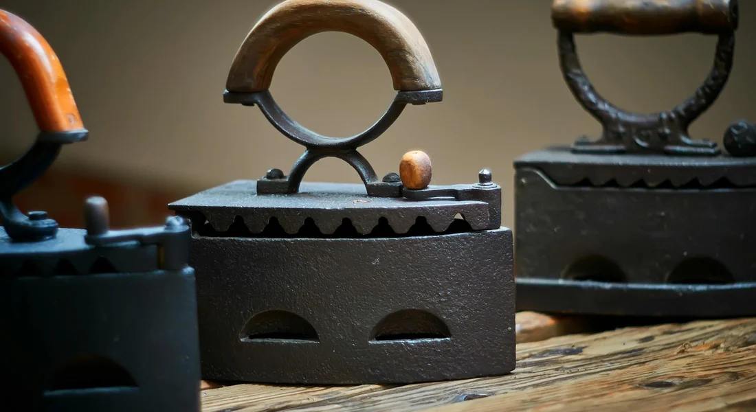 Close-up of three vintage cast-iron irons with wooden and metal handles on a wooden surface, showing rust and wear.