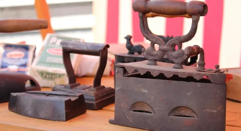 Three antique cast-iron irons on a wooden surface with a colorful striped background.