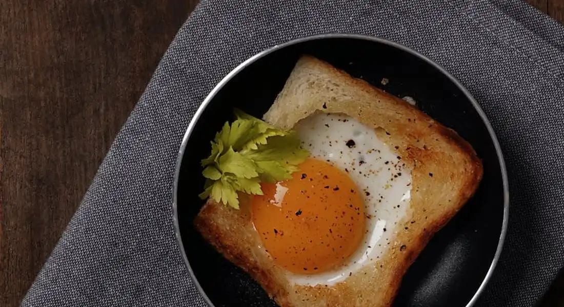 Cast-iron skillet with a fried egg on toast and a sprig of parsley, resting on a gray cloth.