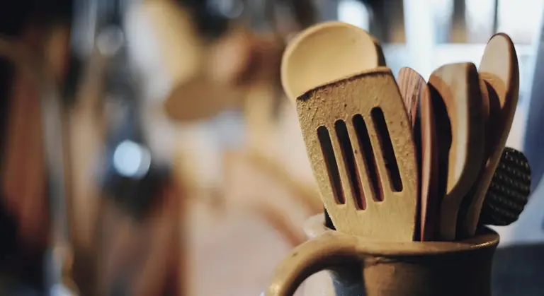 Wooden spatulas and spoons tucked into a ceramic mug with a blurred kitchen background