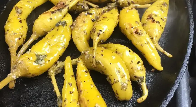 Yellow peppers roasted in a dark cast iron skillet with char marks and seasoning residue.